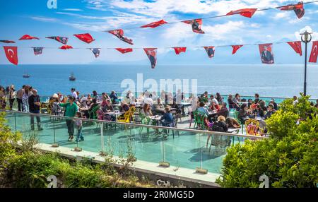 People sit under nationalistic bunting and enjoy panoramic views of the bay and harbour from an outdoor café situated on the ancient walls surrounding Stock Photo