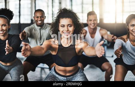 Exercise is too beneficial not to be doing it. a group of young people doing squats together during their workout in a gym. Stock Photo