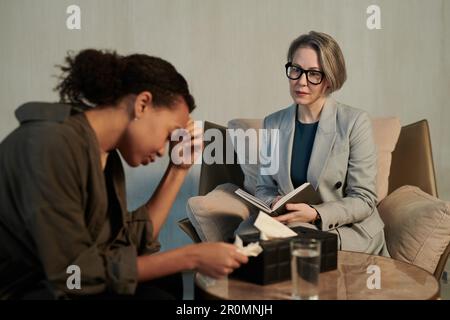 Focus on confident mature female psychologist looking at stressed patient with handkerchief in hand describing her problem during session Stock Photo