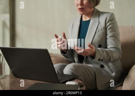 Focus on hands of confident psychologit in grey formalwear explaining something to online patient during session in front of laptop Stock Photo