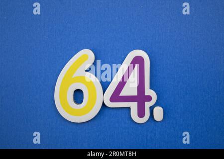 The number 64, placed on a blue background, photographed from above, colored yellow and purple. Stock Photo