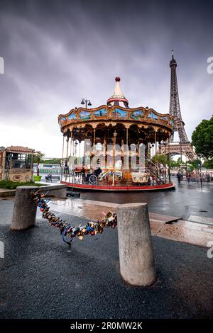 Carousel in front of the Eiffel Tower in rainy weather; in the foreground, love-locks are fastened to the chain of street-bluffing; Paris; Île-de-fran Stock Photo