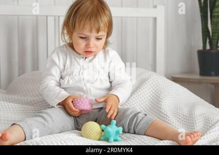 Cute baby girl playing tactile knobby balls. Young child hand plays sensory massage ball. Enhance the cognitive, physical process. Brain development. Stock Photo