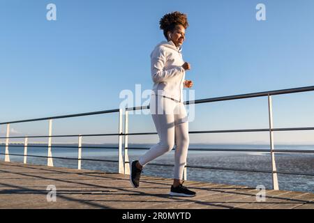 Seaside Run. Young Black Woman Jogging On Wooden Pier Near Sea Stock Photo
