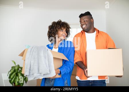 Moving Day. Black Spouses Holding Cardboard Boxes In Hands While Relocating Home Stock Photo
