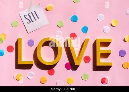 Creative self love text design inscribed on bright pastel pink background decorated with small pieces of colored papers Stock Photo