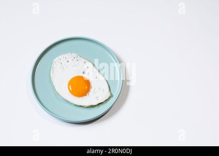 Top view of delicious breakfast of fried egg with yellow yolk served on blue ceramic plate on table against white background Stock Photo