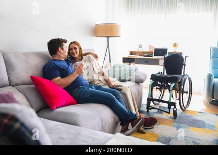Loving couple cuddling and relaxing together on comfortable sofa in living room while talking Stock Photo