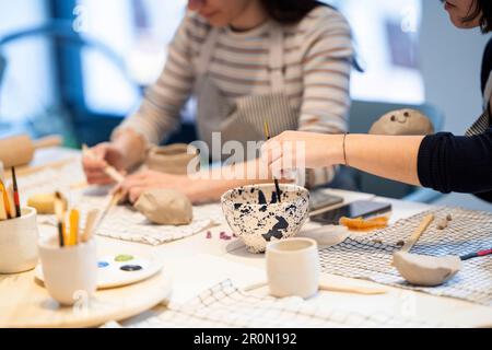 Anonymous female artists in aprons painting on ceramic cups while working in creative pottery studio together Stock Photo