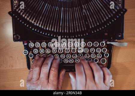From above shot of hands of anonymous elderly person typing on keyboard of vintage typewriter Stock Photo