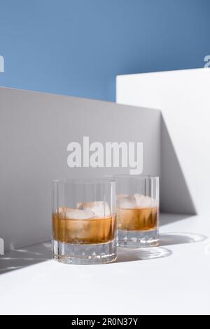 Close up of translucent glasses filled with cold refreshing scotch whiskey with ice cubes placed on white surface against white wall Stock Photo