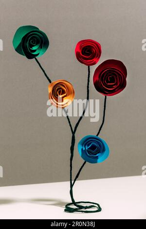 Creative decoration made with colorful paper flowers and wire placed on white table against gray background Stock Photo