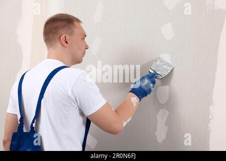 Man plastering wall with putty knife indoors. Home renovation Stock Photo