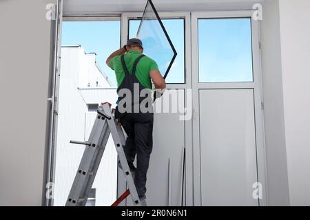Worker on folding ladder installing window indoors Stock Photo