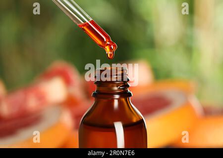 Dripping citrus essential oil from pipette into bottle on blurred background, closeup Stock Photo