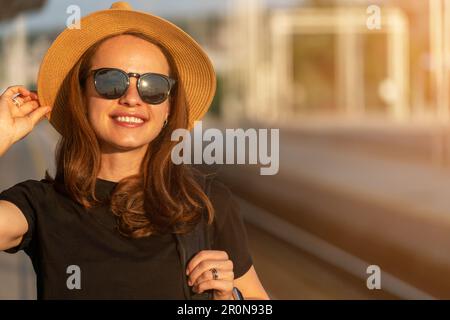 Portrait of brunette woman with tanned skin in straw hat and sunglasses in city. Stock Photo