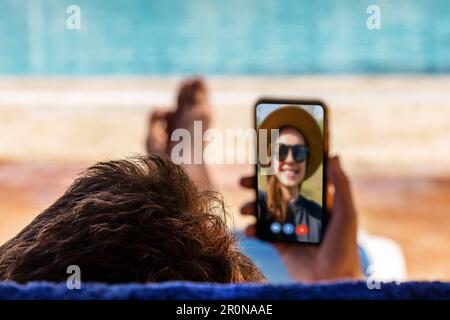 Man calls his girlfriend on video while relaxing near the pool, differential focus. Stock Photo