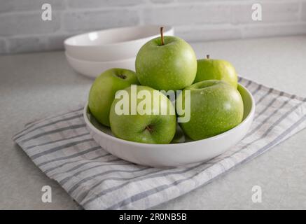 Green apples in a white bowl on kitchen table Stock Photo