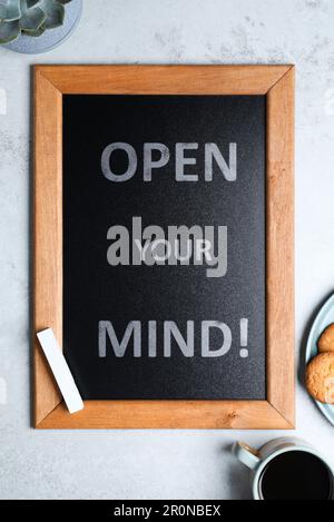 Small chalkboard with motivational quote Open your mind, coffee and cookies on light grey table, flat lay Stock Photo