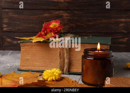 Book decorated with chrysanthemum flowers, autumn leaves and scented candle on light gray textured table Stock Photo