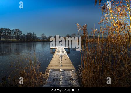 View of a frozen pond with a footbridge in the foreground. Das Blaue Land, Murnau am Staffelsee, Bavaria, Germany Stock Photo