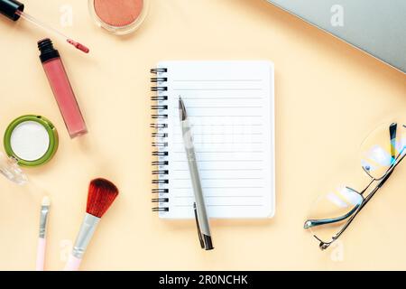 Blank notepad with pen, glasses, notebook and makeup cosmetics on beige background. Beauty blogger concept. Top view, flat lay. Stock Photo