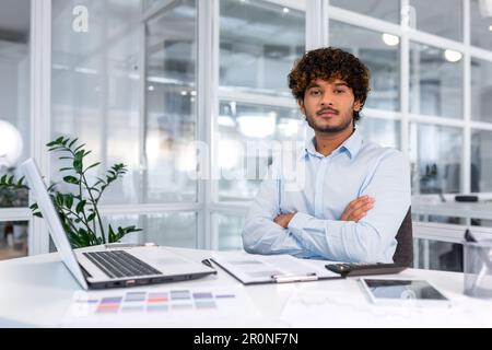 Portrait of serious and confident financier businessman with crossed arms thinking looking at camera, successful hispanic man working inside financial company office with documents, using calculator Stock Photo