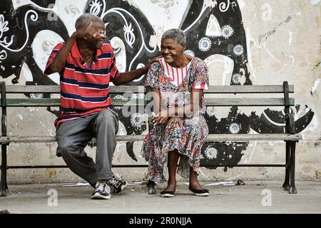 2 friends are chatting and laughing on a street bench in the capital of Cuba. Havana Stock Photo
