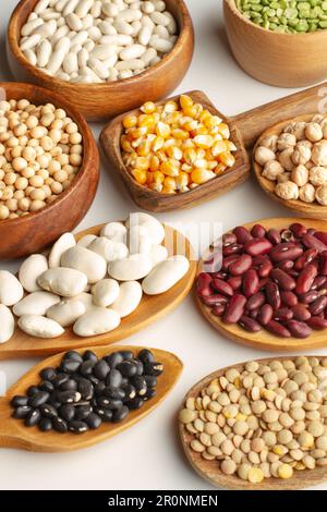 Beans, lentils, chickpeas, soybeans and corn kernels in wooden spoons and bowls on  a white background Stock Photo