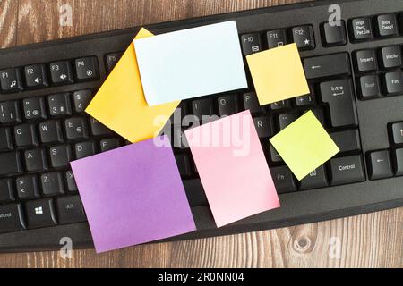 A black computer keyboard with colored paper notes on a wooden desk un a top view Stock Photo