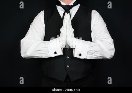 Portrait of Butler in Black Vest and White Gloves Holding Hands in Prayer. Service Industry and Professional Respect and Courtesy. Stock Photo