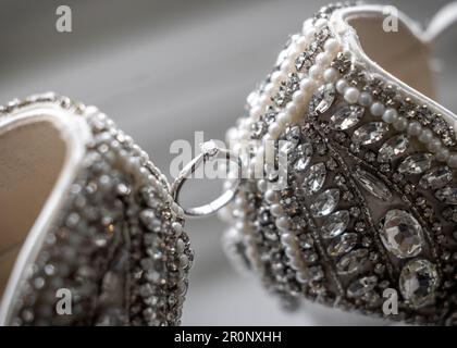 Beautiful diamond solitaire wedding engagement ring held between stunning jewel encrusted high heel shoes Stock Photo