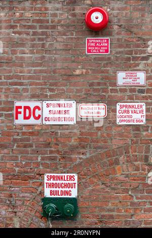 Close up view of a red brick wall with scattered on facade large number of signs to inform about sprinklers, fire, connections, shut off valve Stock Photo