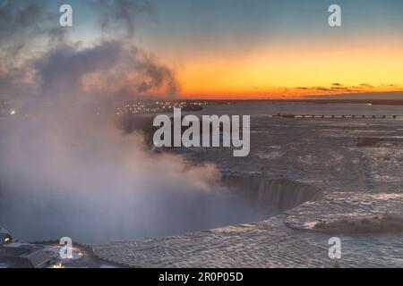 Panoramic view over the Niagara Falls, ON, Canada during winter sunrise with orange sky, water spray from the falls and International Control Dam Stock Photo
