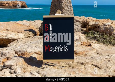 BOM bill of materials symbol. Concept words BOM bill of materials on beautiful black chalk blackboard. Beautiful stone beach sea background. Business Stock Photo