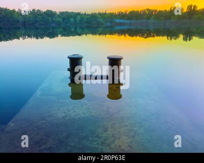 Mooring bollard on the mole with sunset river. Bollard is a mooring device. Two steel cabinets with a common base Stock Photo