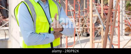 Portrait of young man is engineer wearing helmet smile with satisfied at construction site, architect or contractor standing and thumbs up with confid Stock Photo
