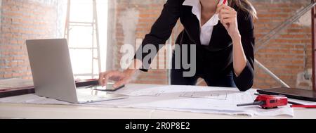 Young caucasian architect woman looking laptop and working drawing blueprint for planning building house on desk, engineer thinking and sketching blue Stock Photo
