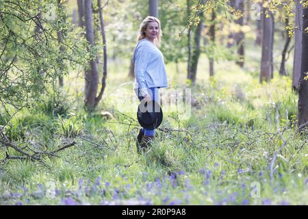 A woman walking in a bluebell wood holding a hat Stock Photo