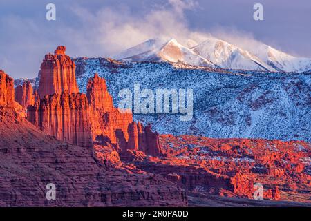 The last golden light of sunset hits the red rocks of Fisher Towers, in front of the La Sal Mountains with fresh snow blowing off the peaks, near Moab Stock Photo
