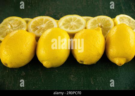 row of whole and sliced lemons creating a border on a green rustic textured background Stock Photo