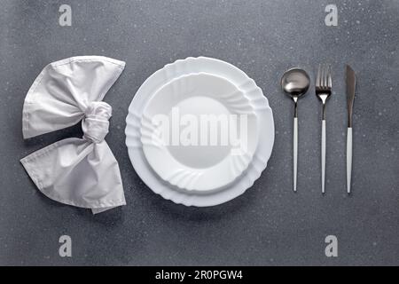 Place setting with white napkin, empty plate and silver cutlery on a gray concrete grunge table. Top view. Festive dinner in a cafe. Menu template, fl Stock Photo