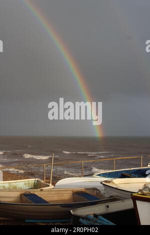 SIDMOUTH, DEVON, UK - MARCH 2, 2017 rainbow over the sea with dark clouds and fishing boats Stock Photo