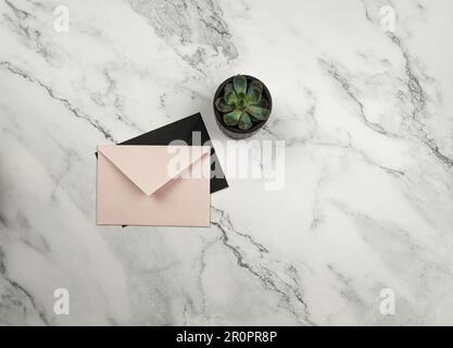 Top view of pink and black envelope on white marble background with green plant. Envelopes and succulent plant flat lay. Copy space. Stock Photo