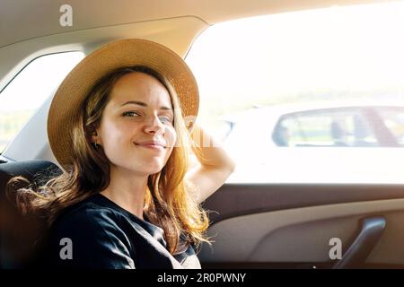 Young woman wearing straw hat enjoying travel by car. Stock Photo