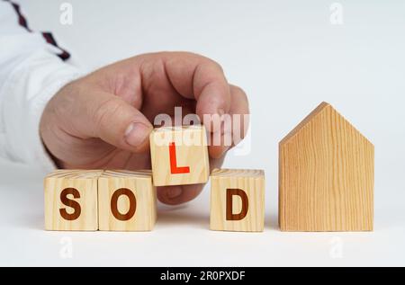 Real estate concept. On a white surface there is a model of a house, next to it a man has placed cubes with the inscription - SOLD Stock Photo