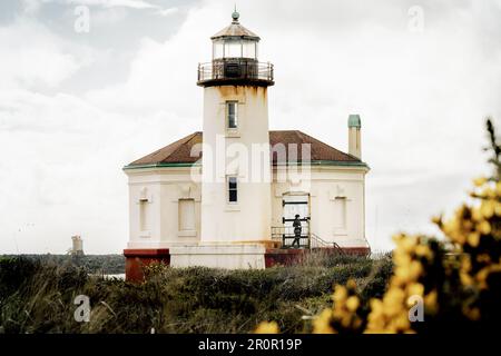 Coquille River Lighthouse in Bandon Oregon USA in Bullards Beach State Park on Oregon Coast PNW on bright overcast day. Horizontal image of woman walk Stock Photo