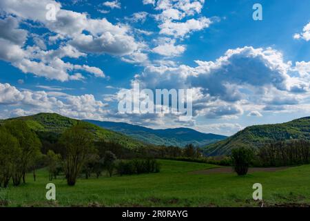 A landscape of nature with sunlit hills and meadows, accompanied by white fluffy clouds in the sky on a sunny spring day Stock Photo