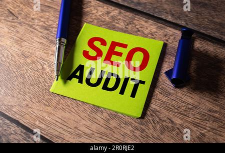 On a light-colored office table is a computer, a black calculator, a pen, and a notebook with the text SEO AUDIT. Business concept. Stock Photo