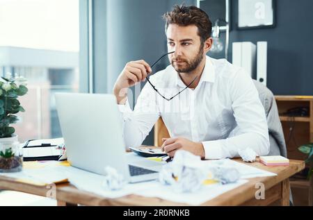 Its been one long and annoying day at the office. a young businessman looking stressed out while working on a laptop in an office. Stock Photo